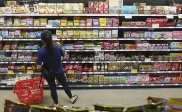 Consumidor selecciona jitomates y papas en un mercado popular mexicano mientras consulta precios de la canasta basica